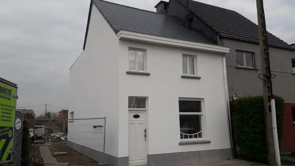 Woning na gevelrenovatie met buitenisolatie, minerale crepi en blauwe hardsteen plinten.